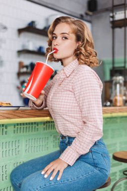 Genç güzel bayan gömlek ve barda oturan kot counter ve düşünceli kamera kafede bakarken soda su içme