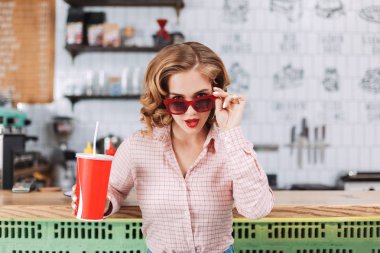 Barda oturan güneş gözlüğü güzel Bayan portresi soda kamera seyir kafede elinde ve sersem su ile karşı