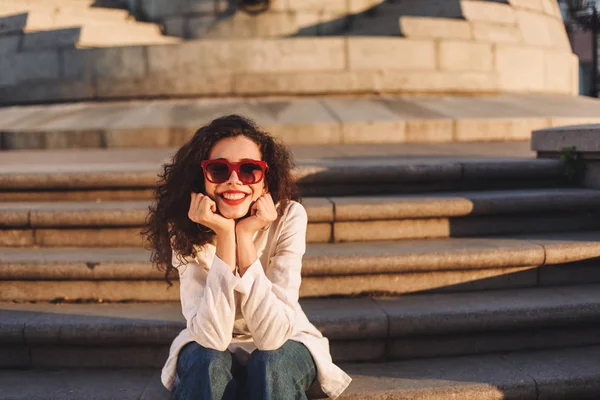 Young Cheerful Lady Dark Curly Hair Sunglasses White Jacket Sitting — Stock Photo, Image