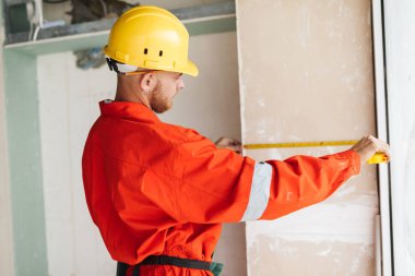 Turuncu iş elbiseleri ve iş ölçüm bandı kullanarak sarı hardhat genç Oluşturucu