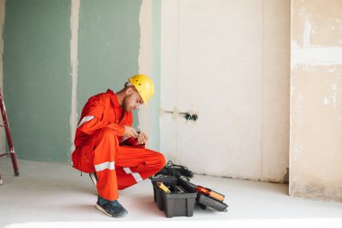 Foreman turuncu iş elbiseleri ve sarı hardhat düşünceli çalışması için araçları seçme 