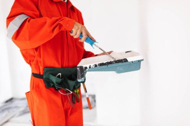 Foreman'ın iş yerinde beyaz boya ile resim rulo kullanarak turuncu iş elbiseleri içinde yukarı kapatın