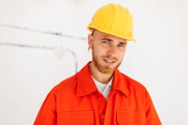 Turuncu genç gülümseyen oluşturucusunun portre çalışmak giysi ve sarı kask kalem mutlu kamera izole seyir kulağının arkasında 