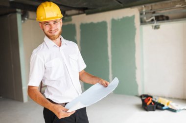 Beyaz gömlek ve sarı hardhat sevinçle yeni daire iş planı üzerinde seyir gülümseyen mimar