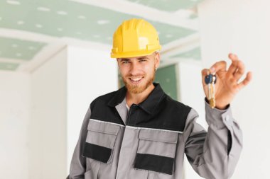 Gülümseyen mühendisi iş elbiseleri ve sarı hardhat mutlu holding tuşları yeni daire el kamera seyir olarak portresi 
