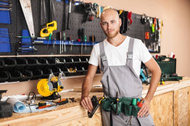 Çalışmalarında genç foreman holding zımba düşünceli kamera arka plan atölye farklı araçlar Ayaklıklı bakıp el giysiler