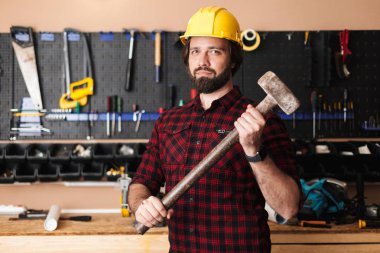 Sarı işçisi holding Builder'da çekiç elinde mutlu kamera araçları Ayaklıklı arka plan atölye üzerinde seyir