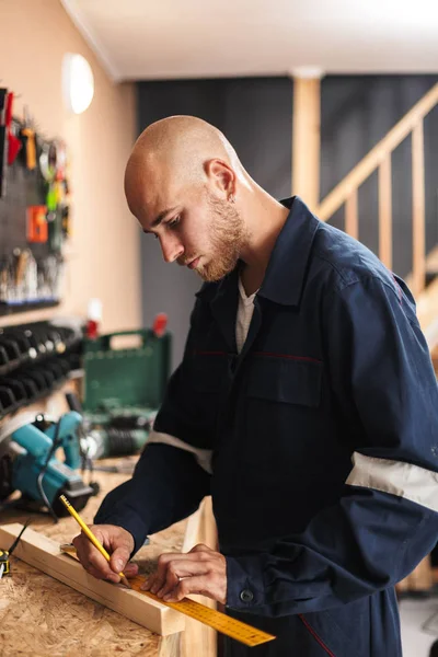 Young foreman in work clothes dreamily using measuring tape in workshop