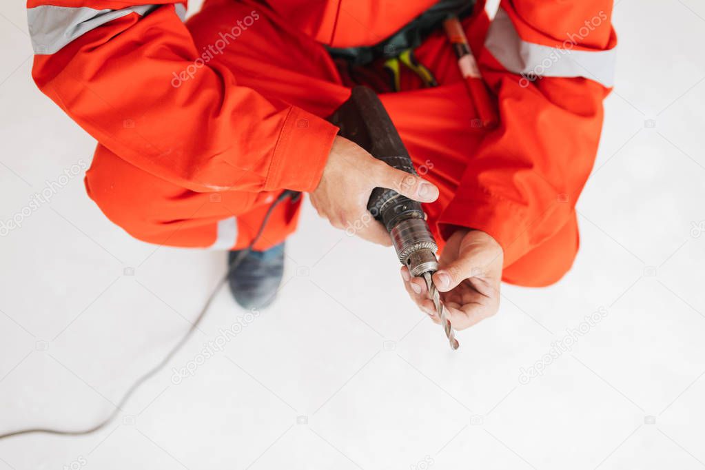 Close up foreman in orange work clothes holding drill machine in hands at work isolated