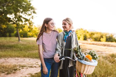 Bisiklet ve sepet kır çiçekleri ve mutlu bir şekilde birbirlerine parkta vakit seyir meyve dolu iki güzel gülümseyen kız