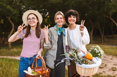 Bisiklet ve sepetleri meyve ve mutlu bir şekilde zafer jestleri gösterilen ve kamera parkta seyir kır çiçekleri ile güzel gülümseyen kız