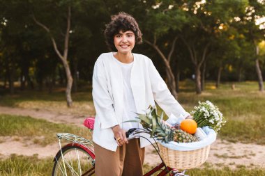 Çok gülümseyen kız klasik bisiklet ve meyve ve sevinçle seyir fotoğraf makinesindeki harcama zaman parkta kır çiçekleri sepeti