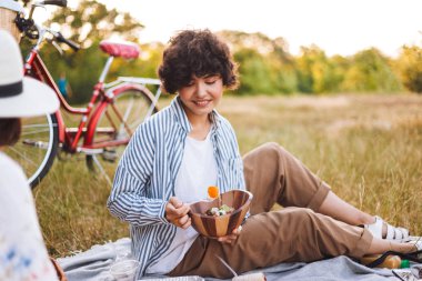 Güzel gülümseyen kız mutlu arkadaşıyla parkta piknik üzerinde vakit salata ile kase tutarak çizgili gömlekli