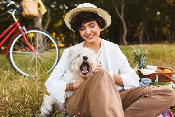 漂亮的女孩在帽子举行可爱的狗快乐地花时间在公园与自行车的背景下的野餐 — 图库照片