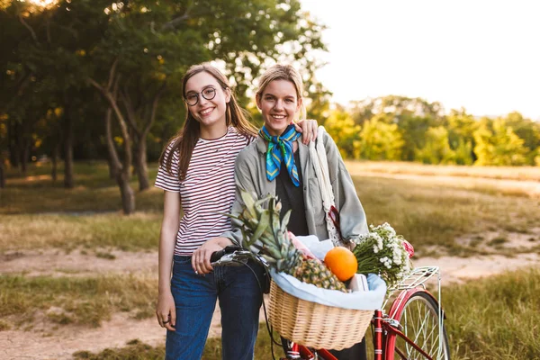 Dwa Ładne Uśmiechający Się Dziewczyny Roweru Kosz Pełen Kwiatów Owoców — Zdjęcie stockowe