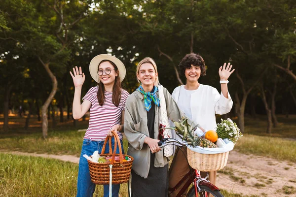 Bisiklet ve tam kır çiçekleri ve mutlu bir şekilde sallayarak ve kamera parkta seyir meyve sepetleri ile oldukça gülümseyen kız grubu