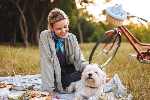 漂亮的微笑的女孩抚摸可爱的小狗愉快地花时间在公园野餐与红色自行车背景 — 图库照片