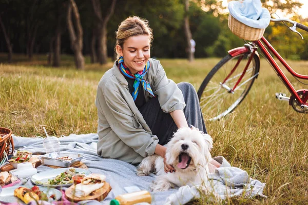 愉快的微笑的女孩与可爱的狗愉快地花费时间在美丽的野餐公园与红色自行车在背景上 — 图库照片
