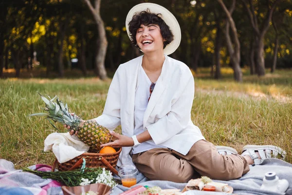 Ananas park piknik vakit elinde tutan şapka ve beyaz gömlekli oturan neşeli kız
