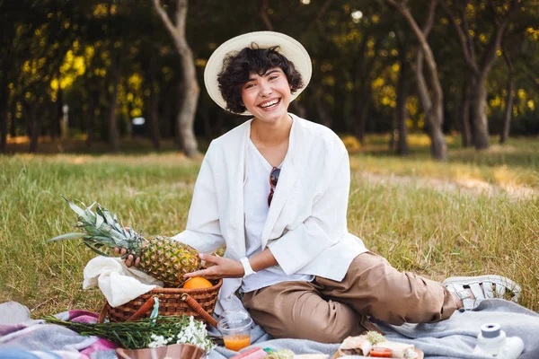 Ananas mutlu kamera park piknik seyir elinde tutan şapka ve beyaz gömlekli oturan güzel gülümseyen kız