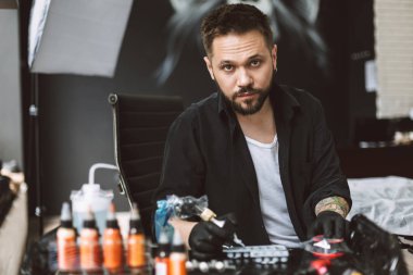 Siyah eldiven düşünceli dövme makinesi modern tattoo Studio elinde tutan kamera seyir profesyonel tattooer 