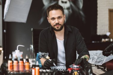 Tattooer sersem dövme makinesi modern tattoo Studio elinde tutan kamera seyir siyah eldiven gülümseyen
