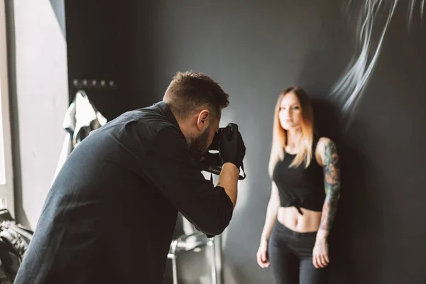 モダンなタトゥー スタジオで黒の背景の上に立っての刺青の女の子のカメラで写真を撮ってタトゥー マスター — ストック写真
