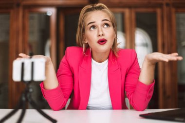 Düşünceli kız pembe ceket amazedly bir yana kayıt yeni video cep telefonunuzun vlog için arıyorsunuz