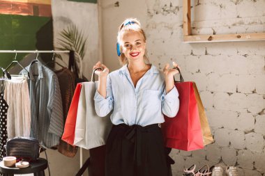 Güzel gülümseyen kız mutlu kamera modern giysiler galeride vakit ellerini tutarak renkli alışveriş torbaları arıyorsunuz
