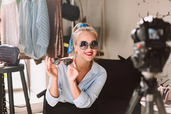 美丽的微笑时尚博客在太阳镜愉快地寻找相机录制新的时尚视频沃客与衣架背景 — 图库照片