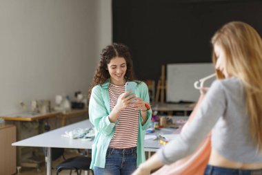 Modern dikiş Atölyesi cep telefonu üzerinde elinde müşteri yeni elbise ile fotoğrafını çekmek oldukça gülümseyerek terzi