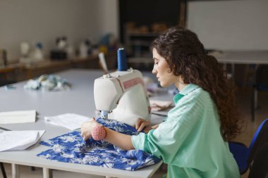 Düşünceli modern dikiş Atölyesi dikiş makinesi kullanarak renkli gömlek siyah kıvırcık saçlı Genç terzi