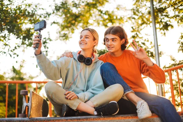 年轻的微笑滑板男孩和女孩与耳机愉快地录制新的视频一起在 Skatepark — 图库照片