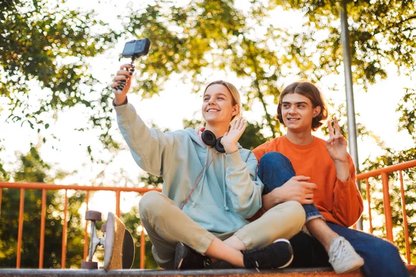 年轻的滑板男孩和女孩与耳机欢快地挥舞着相机录制新的视频在 Skatepark — 图库照片