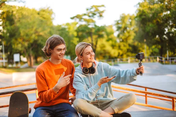 年轻的滑板男孩和女孩与耳机愉快地录制新的视频花时间一起在 Skatepark — 图库照片