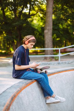 Turuncu kulaklık düşünceli modern skatepark, kaykay ile cep telefonu kullanan genç patenci