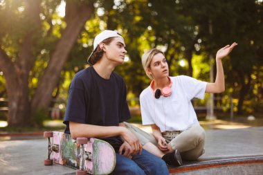Kulaklık ve genç adam düşünceli skatepark, birlikte bir şey tartışırken kaykay ile güzel kız 