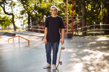 Beyaz şapkalı sersem kamera tutarak kaykay el ile büyük modern skatepark arka plan üzerinde seyir genç kaykaycı