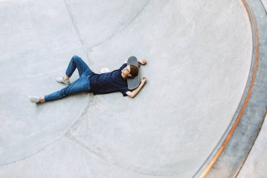 Genç adam sersem modern skatepark, boş kasede kaykay üzerinde yalan