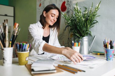 Mutlu bir şekilde harcama zaman evde çizim resimleri ile masaya oturan ressam gülümseyerek 