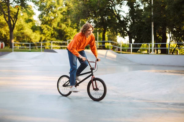 Young Man Orange Pullover Jeans Dreamily Riding Bicycle Modern Skatepark — Stock Photo, Image