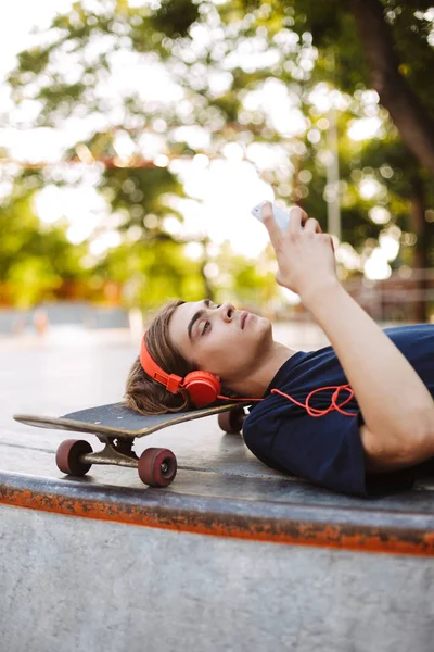 Νεαρός Άντρας Στα Πορτοκαλί Ακουστικά Ξαπλωμένη Για Skateboard Απορώντας Χρησιμοποιώντας — Φωτογραφία Αρχείου