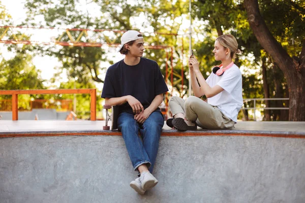Genç adam kaykay üzerinde skatepark birlikte vakit cep telefonu ile fotoğraf çekici kulaklık ile kız gülümseyerek 