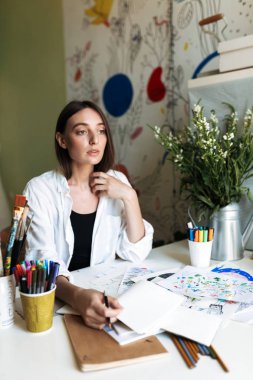 Düşünceli bir yana evde çizim seyir resimlerle masada oturan güzel ressam