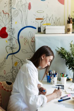 Sersem büyük desenler branda ile evde arka plan üzerinde çizim masasında beyaz gömlekli genç ressam 