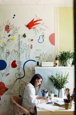 Düşünceli büyük renkli desenler branda ile evde arka plan üzerinde çizim masasında beyaz gömlekli genç ressam