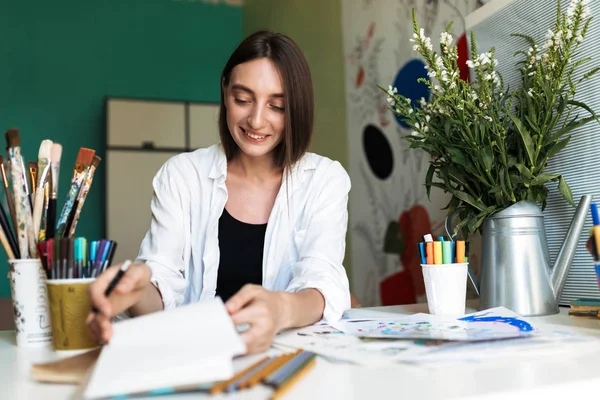 Menina Sorridente Com Cabelo Escuro Sentado Mesa Com Pinturas Alegremente — Fotografia de Stock