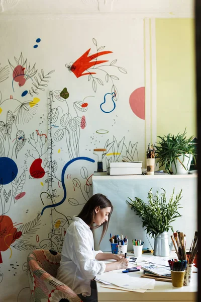 年轻画家在办公桌上的白色衬衫若有所思地绘制与大彩色图案画布在家里的背景 — 图库照片