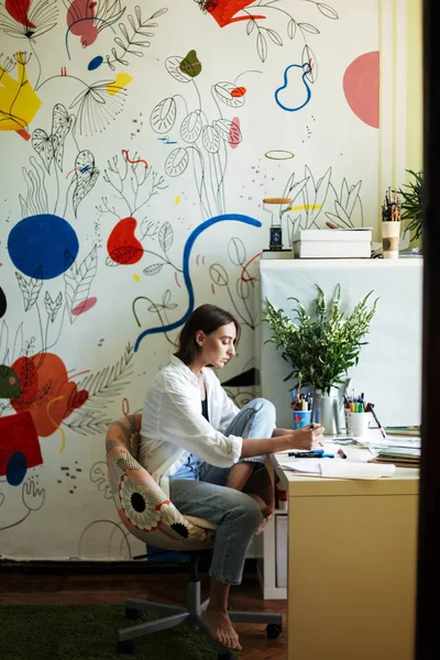 年轻美丽的画家在办公桌上的白色衬衫朦胧的图画与大彩色图案画布在家里的背景 — 图库照片
