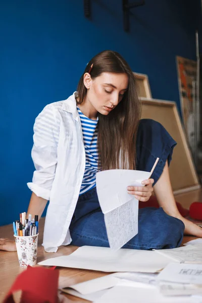 穿着白色衬衫和条纹 T恤的体贴的女孩坐在地板上拿着一张纸 在家里的背景画布 — 图库照片